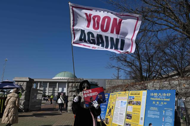 A supporter of South Korea's ousted president Yoon Suk Yeol wave a flag reading "Yoon, Again!" during a rally marking the first anniversary of Yoon's declaration of martial law, in front of the National Assembly in Seoul on December 3, 2025. (Photo by Jung Yeon-je / AFP)