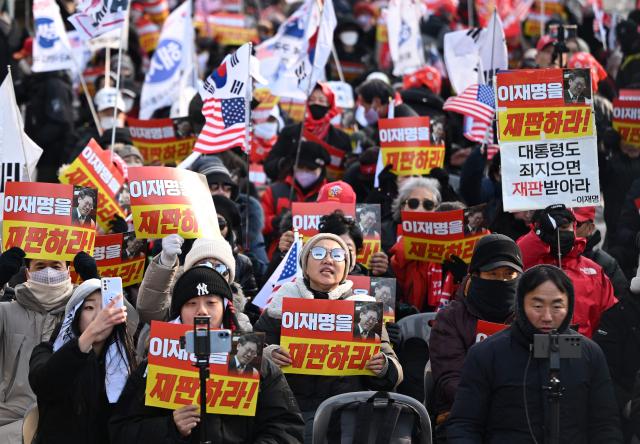 Supporters of South Korea's ousted president Yoon Suk Yeol hold placards reading "Trial Lee Jae Myung!" during a rally marking the first anniversary of Yoon's declaration of martial law, in front of the National Assembly in Seoul on December 3, 2025. (Photo by Jung Yeon-je / AFP)