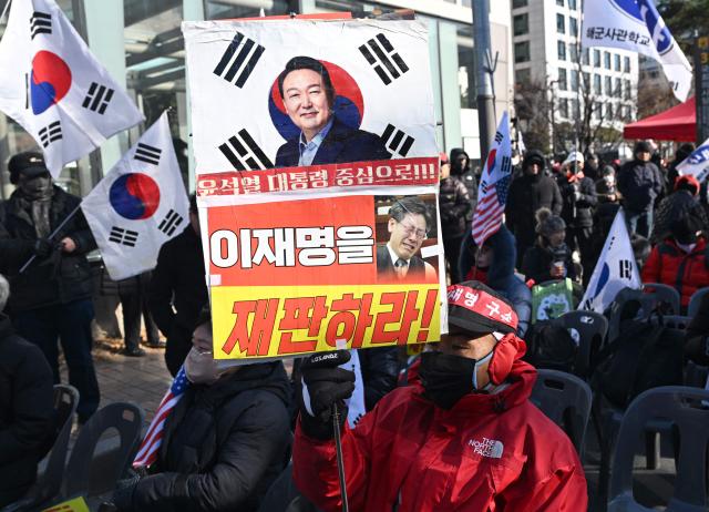 A supporter of South Korea's ousted president Yoon Suk Yeol holds a placard showing a picture of Yoon (top) during a rally marking the first anniversary of Yoon's declaration of martial law, in front of the National Assembly in Seoul on December 3, 2025. (Photo by Jung Yeon-je / AFP)