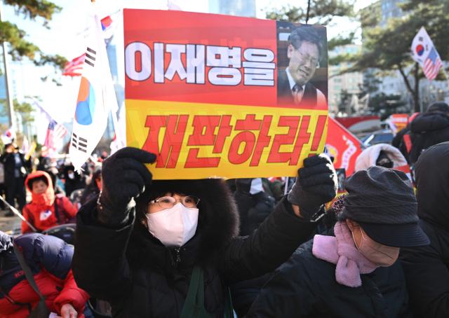A supporter of South Korea's ousted president Yoon Suk Yeol holds a placard reading "Trial Lee Jae Myung!" during a rally marking the first anniversary of Yoon's declaration of martial law, in front of the National Assembly in Seoul on December 3, 2025. (Photo by Jung Yeon-je / AFP)