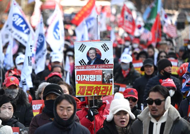 A supporter of South Korea's ousted president Yoon Suk Yeol holds a placard showing a picture of Yoon (top) during a rally marking the first anniversary of Yoon's declaration of martial law, in front of the National Assembly in Seoul on December 3, 2025. (Photo by Jung Yeon-je / AFP)
