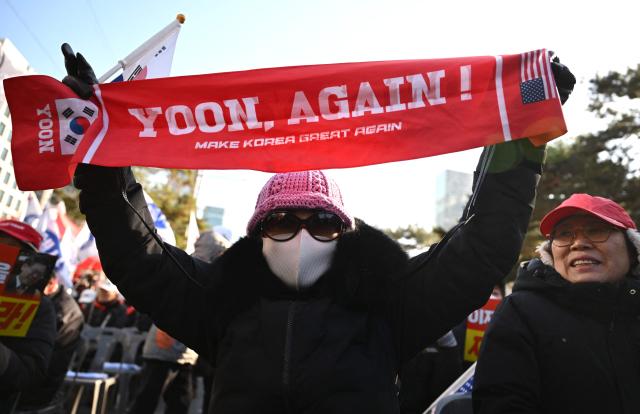 A supporter of South Korea's ousted president Yoon Suk Yeol holds up a red banner reading "Yoon, Again!" during a rally marking the first anniversary of Yoon's declaration of martial law, in front of the National Assembly in Seoul on December 3, 2025. (Photo by Jung Yeon-je / AFP)
