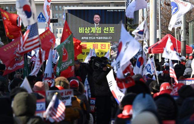Supporters of South Korea's ousted president Yoon Suk Yeol watch a video of Yoon declaring martial law during a rally marking the first anniversary of the declaration of martial law, in front of the National Assembly in Seoul on December 3, 2025. (Photo by Jung Yeon-je / AFP)