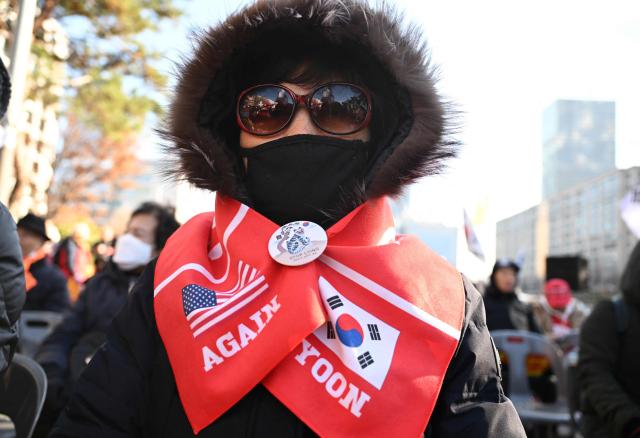 A supporter of South Korea's ousted president Yoon Suk Yeol wears a red banner reading "Yoon, Again" on her shoulder during a rally marking the first anniversary of Yoon's declaration of martial law, in front of the National Assembly in Seoul on December 3, 2025. (Photo by Jung Yeon-je / AFP)