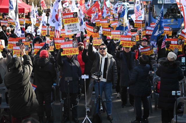 Supporters of South Korea's ousted president Yoon Suk Yeol hold placards reading "Trial Lee Jae Myung!" during a rally marking the first anniversary of Yoon's declaration of martial law, in front of the National Assembly in Seoul on December 3, 2025. (Photo by Jung Yeon-je / AFP)