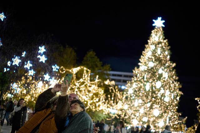 People take a selfie in front of a christmas tree at Suntagma square in Athens on December 2, 2025. (Photo by Aggelos NAKKAS / AFP)