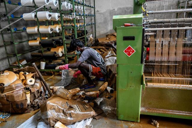 A man salvages raw materials next to a power loom at an inundated factory following flash floods in the aftermath of Cyclone Ditwah, in Wellampitiya on the outskirts of Colombo on December 3, 2025. Sri Lankan authorities said on December 3 they would need some $7 billion to rebuild homes, industries and roads destroyed by Cyclone Ditwah, which has left at least 465 people dead so far. (Photo by Ishara S. KODIKARA / AFP)