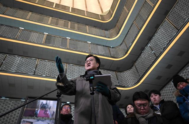 National Assembly Speaker Woo Won-shik (C) guides visitors during a dark tour on martial law sites to mark the first anniversary of the declaration of martial law by ousted president Yoon Suk Yeol, at the National Assembly in Seoul on December 3, 2025. Yoon suspended civilian rule in South Korea on December 3, 2024, for the first time in more than four decades, prompting massive protests and a showdown in parliament. A year later, the country remains politically polarised as it faces a slowing economy and an ageing population, as well as the lingering threat from North Korea. (Photo by JUNG YEON-JE / POOL / AFP)