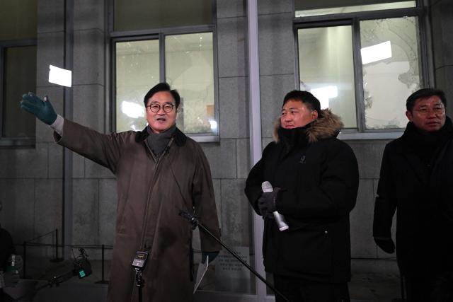 National Assembly Speaker Woo Won-shik (L) speaks in front of the windows that were broken when soldiers stormed the National Assembly building a year ago, as he guides visitors during a dark tour on martial law sites to mark the first anniversary of the declaration of martial law by ousted president Yoon Suk Yeol, at the National Assembly in Seoul on December 3, 2025. Yoon suspended civilian rule in South Korea on December 3, 2024, for the first time in more than four decades, prompting massive protests and a showdown in parliament. A year later, the country remains politically polarised as it faces a slowing economy and an ageing population, as well as the lingering threat from North Korea. (Photo by JUNG YEON-JE / POOL / AFP)