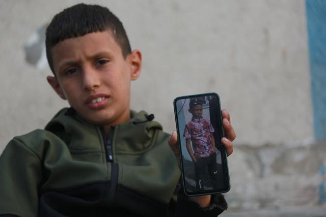 Nine-years-old Rateb Mahmoud Qaliq, originally from the Bedouin village in the northern Gaza Strip, and currently displaced with his grandfather, holds a mobile phone with an image of himself prior to his injury, at an UNRWA school that has become a shelter for displaced people in Deir al-Balah, in the central Gaza Strip on December 3, 2025. Rateb was injured in Khan Yunis, in the southern Gaza Strip on June 28, 2025, while visiting his grandfather's tent when a nearby car was bombed by the Israeli military as he, his mother, and his brother were walking past. His mother and brother were killed, and his leg was was damaged and later amputated. Rateb suffers from a misaligned prosthetic leg and rarely uses it because it is uncomfortable, finding his crutches lighter and more comfortable. The war was sparked by Hamas's October 7, 2023 attack on Israel, which resulted in the deaths of 1,221 people. Israel's retaliatory assault on Gaza has killed over 70,000 people, according to figures from the health ministry that the UN considers reliable. (Photo by Bashar Taleb / AFP)