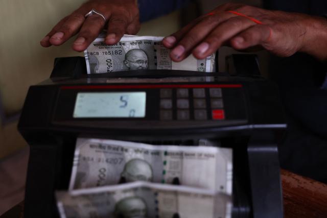 A vendor uses a cash counting machine at a market in Varanasi on December 3, 2025. India's rupee fell to a fresh record low of over 90 per dollar on December 3, extending recent declines, with traders partly blaming the delay in striking a trade deal with the United States. (Photo by Niharika KULKARNI / AFP)