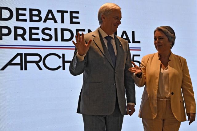 Chile's presidential candidate Jose Antonio Kast (L), of the Partido Republicano party, waves as Chile's presidential candidate Jeannette Jara, of the Unidad por Chile coalition, extends her hand before a debate organised by the Chilean Radio Association (Archi) in Santiago, on December 3, 2025. The clock is ticking down to a presidential run-off election on December 14, with far-right candidate Jose Antonio Kast the frontrunner to win the second round of voting against leftist Jeannette Jara. (Photo by RODRIGO ARANGUA / AFP)