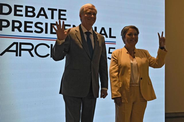 Chile's presidential candidate Jose Antonio Kast (L), of the Partido Republicano party, waves as Chile's presidential candidate Jeannette Jara, of the Unidad por Chile coalition, flashes the V sign before a debate organised by the Chilean Radio Association (Archi) in Santiago, on December 3, 2025. The clock is ticking down to a presidential run-off election on December 14, with far-right candidate Jose Antonio Kast the frontrunner to win the second round of voting against leftist Jeannette Jara. (Photo by RODRIGO ARANGUA / AFP)