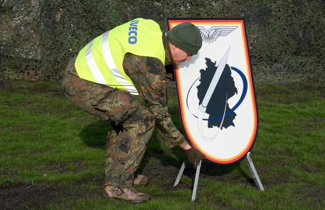 A German soldier sets up a sign depicting a rocket surrounding a map of Germany during an event of the German Air Force to declare the Initial Operating Capability for the Arrow Weapon System for Germany at the Annaburger Heide Air Base in Schoenewalde / Holzdorf, eastern Germany, on December 3, 2025. The German military put the first parts of a roughly $4 billion Arrow 3 anti-missile shield system into service, aimed at bolstering Europe's air defences to counter Russian threats. The Arrow 3 shield system is part of the broader European Sky Shield effort launced in the wake of Russia's full-scale invasion of Ukraine, which raised alarm over possible gaps in NATO's European air defences. The German-Israeli deal to supply the Arrow 3 system inked in 2023 has been described as Israel's largest-ever military export contract. (Photo by RALF HIRSCHBERGER / AFP)