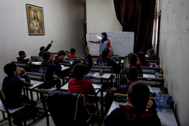 An educator to points to a young learner during the start of classes at Latin Patriarchate School inside the Holy Family Catholic Church compound sheltering displaced Palestinians in Gaza City, on December 3, 2025. Israel said on December 3, it would open the Rafah crossing from Gaza to Egypt to allow residents to exit the Palestinian territory "in the coming days," but Egypt denied such a deal with Israel. (Photo by Omar AL-QATTAA / AFP)