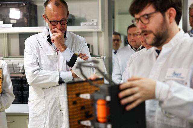 German Chancellor Friedrich Merz (L) and Berlin's Mayor Kai Wegner (covered) look at a satellite system during their visit at Berlin Space Technologies (BST) in Adlershof district, in Berlin, Germany, during Merz' first official visit as Chancellor to the federal state of Berlin on December 3, 2025. (Photo by Nadja Wohlleben / POOL / AFP)