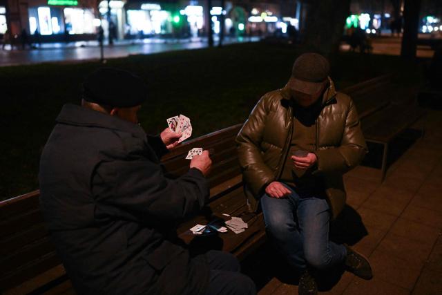 Two residents play cards in the street in Lviv on December 3, 2025, amid the Russian invasion of Ukraine. (Photo by Sergei GAPON / AFP)