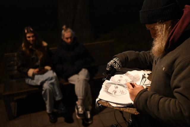 A street artist draws a sketch of two women in the street in Lviv on December 3, 2025, amid the Russian invasion of Ukraine. (Photo by Sergei GAPON / AFP)