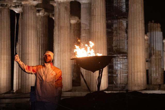 Greek rower Stefanos Ntouskos holds the Olympic flame in front of the ancient temple of the Parthenon atop the Acropolis hill during the Olympic torch relay in Athens on December 3, 2025. (Photo by Angelos TZORTZINIS / AFP)