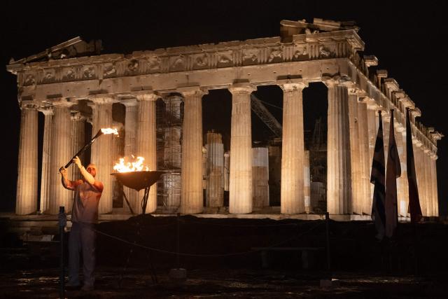Greek rower Stefanos Ntouskos lights a cauldron with the Olympic flame in front of the ancient temple of the Parthenon atop the Acropolis hill during the Olympic torch relay in Athens on December 3, 2025. (Photo by Angelos TZORTZINIS / AFP)