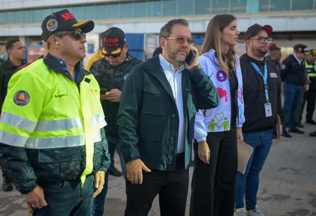 Venezuela's Foreign Minister Yvan Gil uses his phone as he waits for an Eastern Airlines plane carrying Venezuelan migrants repatriated from the US at Simon Bolivar International Airport in Maiquetia, Venezuela, on December 3, 2025. Venezuela announced on December 2, 2025, that it had reauthorized flights carrying migrants deported by the US, days after suspending them due to President Donald Trump's demand that Venezuelan airspace be considered "closed." (Photo by Juan BARRETO / AFP)