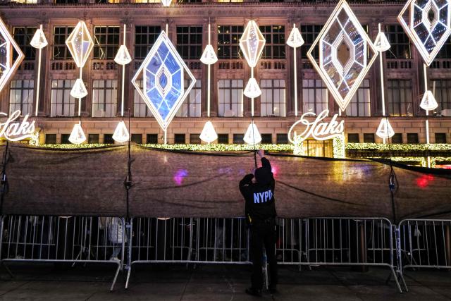 A NYPD officer helps install a cover to prevent pedestrians to stop and look the Christmas tree, blocking adjacent sidewalks, during the Rockefeller Center Christmas Tree Lighting in New York City on December 3, 2025. (Photo by CHARLY TRIBALLEAU / AFP)