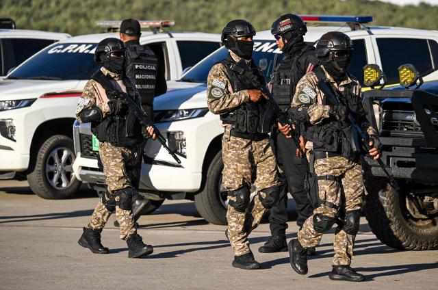 Police officers patrol the tarmac before the arrival of an Eastern Airlines plane carrying Venezuelan migrants repatriated from the US at Simon Bolivar International Airport in Maiquetia, Venezuela, on December 3, 2025. Venezuela announced on December 2, 2025, that it had reauthorized flights carrying migrants deported by the US, days after suspending them due to President Donald Trump's demand that Venezuelan airspace be considered "closed." (Photo by Juan BARRETO / AFP)