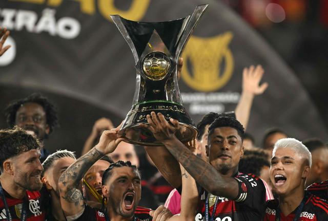 Flamengo's Uruguayan midfielder #10 Giorgian de Arrascaeta (C-L) and forward #27 Bruno Henrique (C-R) lift the Brasileirao trophy after winning the Brasileirao Serie A football match between Flamengo and Ceara at Maracana Stadium in Rio de Janeiro, Brazil, on December 3, 2025. (Photo by Mauro PIMENTEL / AFP)