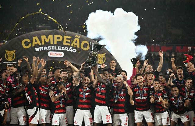 Flamengo's Uruguayan midfielder #10 Giorgian de Arrascaeta (C-L) and forward #27 Bruno Henrique (C-R) lift the Brasileirao trophy after winning the Brasileirao Serie A football match between Flamengo and Ceara at Maracana Stadium in Rio de Janeiro, Brazil, on December 3, 2025. (Photo by Mauro PIMENTEL / AFP)