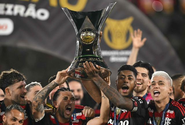 Flamengo's Uruguayan midfielder #10 Giorgian de Arrascaeta (C-L) and forward #27 Bruno Henrique (C-R) lift the Brasileirao trophy after winning the Brasileirao Serie A football match between Flamengo and Ceara at Maracana Stadium in Rio de Janeiro, Brazil, on December 3, 2025. (Photo by Mauro PIMENTEL / AFP)