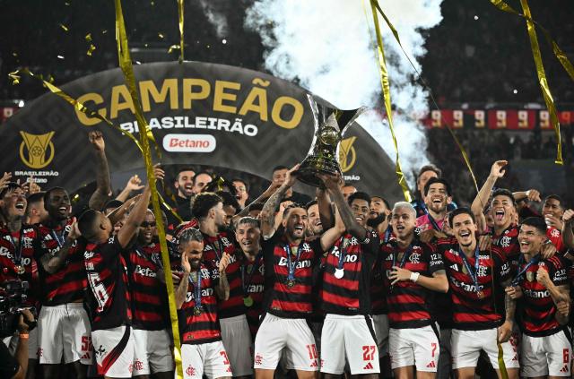Flamengo's Uruguayan midfielder #10 Giorgian de Arrascaeta (C-L) and forward #27 Bruno Henrique (C-R) lift the Brasileirao trophy after winning the Brasileirao Serie A football match between Flamengo and Ceara at Maracana Stadium in Rio de Janeiro, Brazil, on December 3, 2025. (Photo by Mauro PIMENTEL / AFP)
