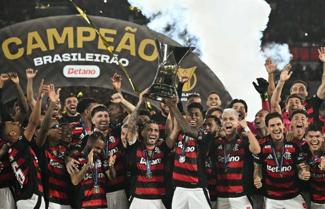 Flamengo's Uruguayan midfielder #10 Giorgian de Arrascaeta (C-L) and forward #27 Bruno Henrique (C-R) lift the Brasileirao trophy after winning the Brasileirao Serie A football match between Flamengo and Ceara at Maracana Stadium in Rio de Janeiro, Brazil, on December 3, 2025. (Photo by Mauro PIMENTEL / AFP)