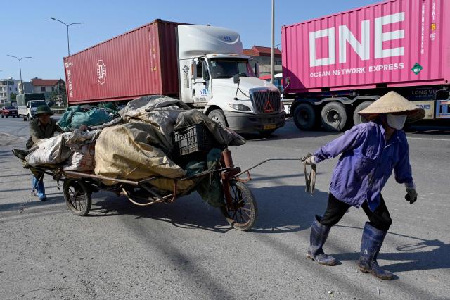 This photo taken on November 25, 2025, shows a couple pushing and pulling a cart carrying plastic waste on a highway in Hung Yen province. (Photo by Nhac NGUYEN / AFP)