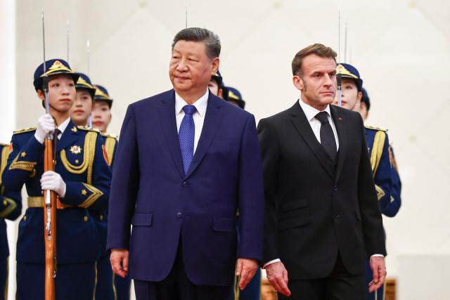 China's President Xi Jinping (L) stands next to France's President Emmanuel Macron during a welcome ceremony at the Great Hall of the People in Beijing on December 4, 2025. (Photo by Sarah Meyssonnier / POOL / AFP)