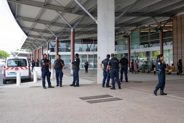 Police officers stand at the entrance of the Noumea - La Tontouta international airport upon arrival of Kanak pro-independence leader Christian Tein (L), head of the CCAT (Cellule de Coordination des Actions de Terrain), in La Tontouta, south of Noumea, in France's Pacific territory of New Caledonia, on December 4, 2025. (Photo by Delphine MAYEUR / AFP)