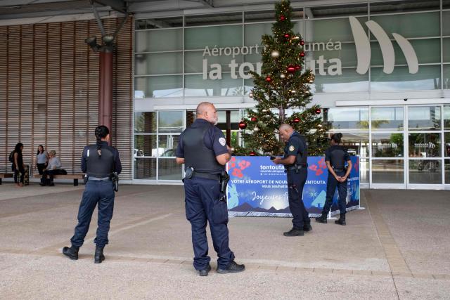 Police officers stand at the entrance of the Noumea - La Tontouta international airport upon arrival of Kanak pro-independence leader Christian Tein (L), head of the CCAT (Cellule de Coordination des Actions de Terrain), in La Tontouta, south of Noumea, in France's Pacific territory of New Caledonia, on December 4, 2025. (Photo by Delphine MAYEUR / AFP)
