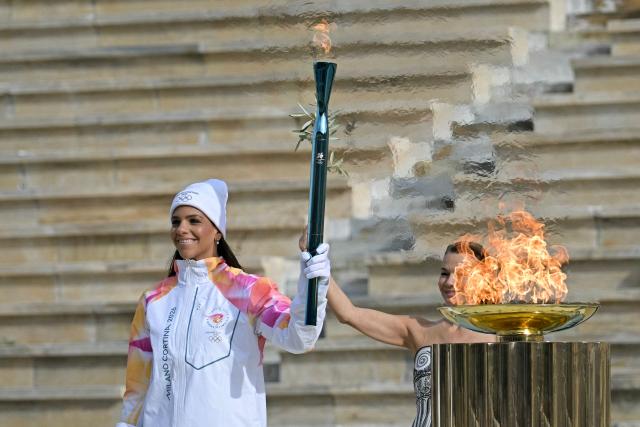 Greek water polo athlete Eleni Xenaki (L) next to Greek actress Mary Mina (R), playing the role of the High Priestess, poses with the Olympic torch during the handover Olympic flame ceremony for the Milano-Cortina 2026 Winter Olympic Games and Paralympic Games, at the Panathinean stadium in Athens, on December 4, 2025. (Photo by Aggelos NAKKAS / AFP)