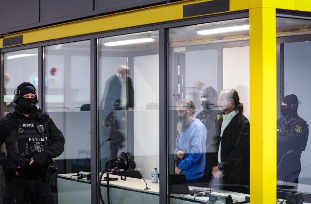 Saudi Arabian defendant Taleb Jawad al-Abdulmohsen (C) stands next to his court-appointed defence lawyers Thomas Rutkowski as he waits inside a bulletproof glass box in the temporary courtroom in Magdeburg, eastern Germany on December 4, 2025, during his trial over the deadly Christmas market attack in December 2024. The Saudi doctor went on trial accused of driving an SUV through a Christmas market, killing six people and wounding more than 300. Taleb Jawad al-Abdulmohsen, a 51-year-old psychiatrist, was arrested next to the battered rental vehicle after the attack on December 20, 2024 in the eastern city of Magdeburg. (Photo by RONNY HARTMANN / AFP)