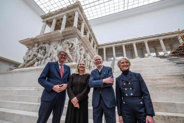 (From L) German State Minister for Culture and Media Wolfram Weimer, President of the Prussian Cultural Heritage Foundation Marion Ackermann, German architect Jan Kleihues and President of the Federal Office for Building and Regional Planning (BBR) Petra Wesseler, pose in front of the Pergamon Altar, as renovation work continues at the Pergamon Museum, in Berlin on December 4, 2025. With the first construction phase completed, the Collection of Classical Antiquities, Museum of Islamic Art, and Museum of the Ancient Near East are expected to reopen to the public  in spring 2027. The Pergamon Museum's complete renovation is expected to be finished in 2037. (Photo by John MACDOUGALL / AFP)