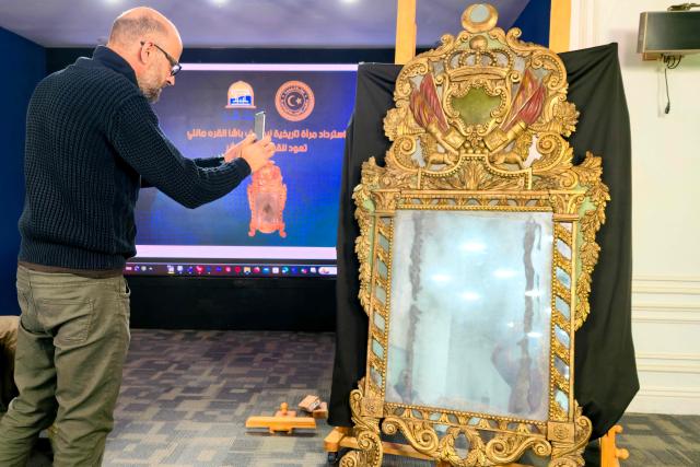 A man takes a picture of a 19th-century mirror once owned by Yusuf Pasha al-Qaramanli that was returned to Libya from the US, after its presentation in Tripoli on December 4, 2025. (Photo by Mahmud Turkia / AFP)