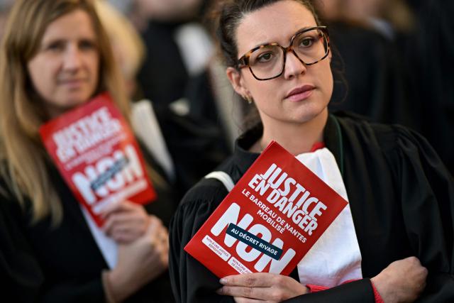 Protesters hold pamphlets reading "Justice in danger - Nantes Bar Association takes action - No to the "RIVAGE" decree" as lawyers gather during a demonstration in front of the Rennes' Court of Appeal to protest against the proposed "RIVAGE" decree (Rationalisation of Appeal Proceedings to Ensure Efficiency) in Rennes, western France, on December 4, 2025. (Photo by Damien MEYER / AFP)