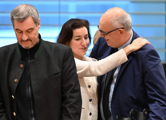 Bavaria's State Premier Markus Soeder (L) looks on as Bremen's mayor Andreas Bovenschulte (R) is hugged by German Minister for Research, Technology and Aerospace Dorothee Baer at the start of a meeting of the leaders of the country's federal states with the German Chancellor on December 4, 2025 at the Chancellery in Berlin. (Photo by RALF HIRSCHBERGER / AFP)