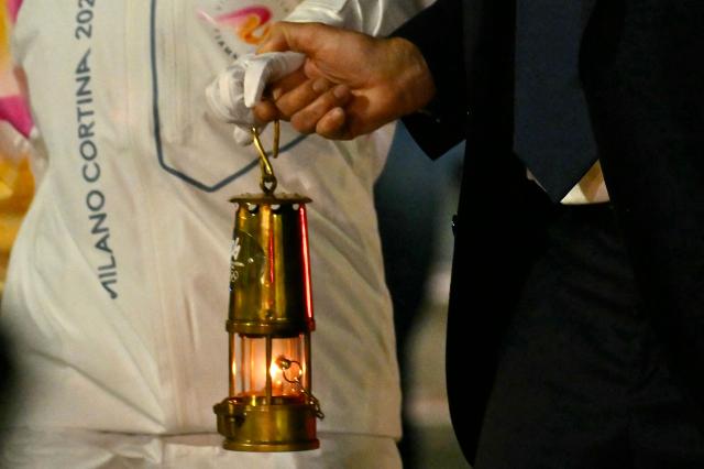 Italian tennis player Jasmine Paolini and Giovanni Malago, President of Fondazione Milano Cortina 2026 hold a lantern with the Olympic flamme at Rome's Fiumicino airport on December 4, 2025.  The torch relay in Italy will start on December 6 ahead of the Milano Cortina 2026 Olympic and Paralympic Games. (Photo by Filippo MONTEFORTE / AFP)