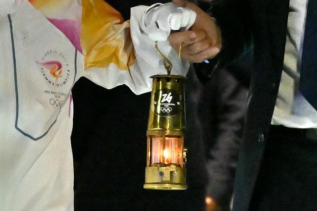 Italian tennis player Jasmine Paolini and Giovanni Malago, President of Fondazione Milano Cortina 2026 hold a lantern with the Olympic flamme at Rome's Fiumicino airport on December 4, 2025.  The torch relay in Italy will start on December 6 ahead of the Milano Cortina 2026 Olympic and Paralympic Games. (Photo by Filippo MONTEFORTE / AFP)