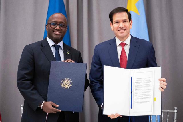 US Secretary of State Marco Rubio (R) and Rwandan Foreign Minister Olivier Nduhungirehe pose with signed agreements during a ceremony at the US Institute of Peace in Washington, DC on December 4, 2025. US President Donald Trump on Thursday brings the leaders of Rwanda and the Democratic Republic of Congo together to endorse a deal that Trump has hailed as his latest peace triumph despite ongoing violence on the ground. Trump hopes the agreement will pave the way for the United States to gain access to critical minerals in the eastern DRC, a violence-torn region home to many of the key ingredients in modern technologies such as electric cars. (Photo by Allison ROBBERT / AFP)
