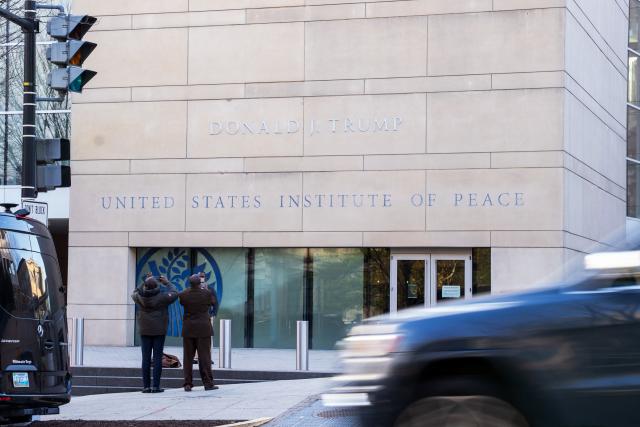 People snap photos outside of the United States Peace Institute, with the recently added name of US President Donald Trump, as a signing agreement ceremony is taking place between Rwanda and the Democratic Republic of the Congo in Washington, DC, on December 4, 2025. Trump on Thursday brings the leaders of Rwanda and the Democratic Republic of Congo together to endorse a deal that Trump has hailed as his latest peace triumph despite ongoing violence on the ground. Trump hopes the agreement will pave the way for the United States to gain access to critical minerals in the eastern DRC, a violence-torn region home to many of the key ingredients in modern technologies such as electric cars. (Photo by Allison ROBBERT / AFP)