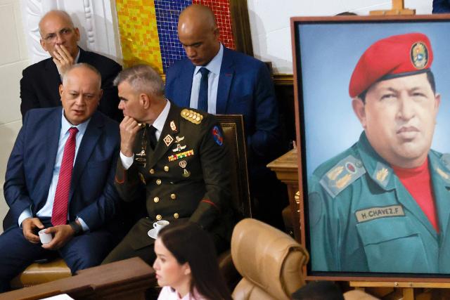 Venezuela's Minister of Interior Relations, Justice and Peace, Diosdado Cabello (L), and  Defense Minister, Vladimir Padrino Lopez (R), talk past a portrait of late Venezuelan President Hugo Chavez during the presentation of the 2026 fiscal year budget at the National Congress in Caracas on December 4, 2025. (Photo by Pedro MATTEY / AFP)