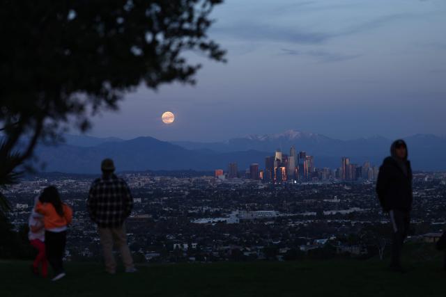 People watch the last supermoon of 2025, the Cold Moon, rising behind the snow-capped San Gabriel Mountains and the Los Angeles skyline as seen from Kenneth Hahn State Recreation Area on December 4, 2025. (Photo by Patrick T. Fallon / AFP)