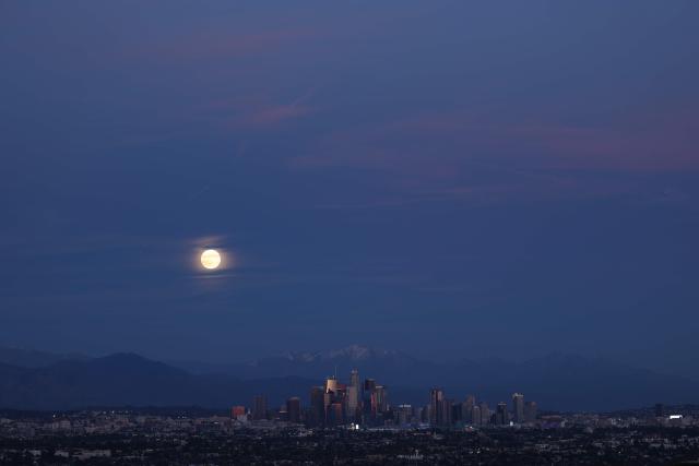 The last supermoon of 2025, the Cold Moon, rises behind the snow-capped San Gabriel Mountains and the Los Angeles skyline as seen from Kenneth Hahn State Recreation Area on December 4, 2025. (Photo by Patrick T. Fallon / AFP)
