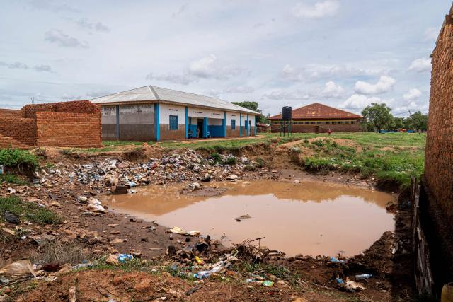 A pool of stagnant water fills the yard outside of a hospital in Lubumbashi on November 24, 2025. Her parched field is overrun with debris carried by polluted waters, and the little girl in his arms is covered in sores: in Lubumbashi, the mining capital of the DRC, thousands of Congolese claim to be victims of toxic waste from the mining industry. Hélène Mvubu recounts enduring for years the effects of floods caused by contaminated water discharged by Congo Dongfang Mining (CDM), a Chinese mining company that processes copper and cobalt ores in the outskirts of the capital of Katanga province, in the southeastern Democratic Republic of Congo (DRC). (Photo by Glody MURHABAZI / AFP)